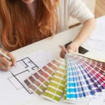 Closeup of woman with red hair and white blouse working on choosing color paint for her house.