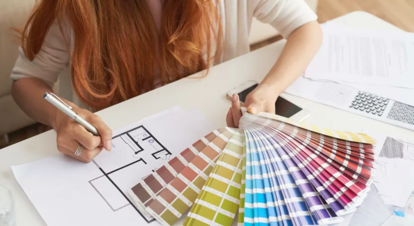 Closeup of woman with red hair and white blouse working on choosing color paint for her house.