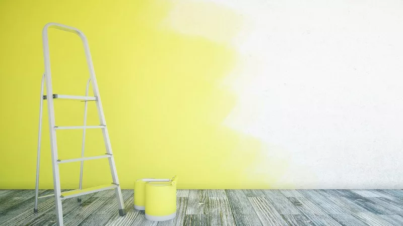 Step ladder and paint cans in front of partially painted interior wall.