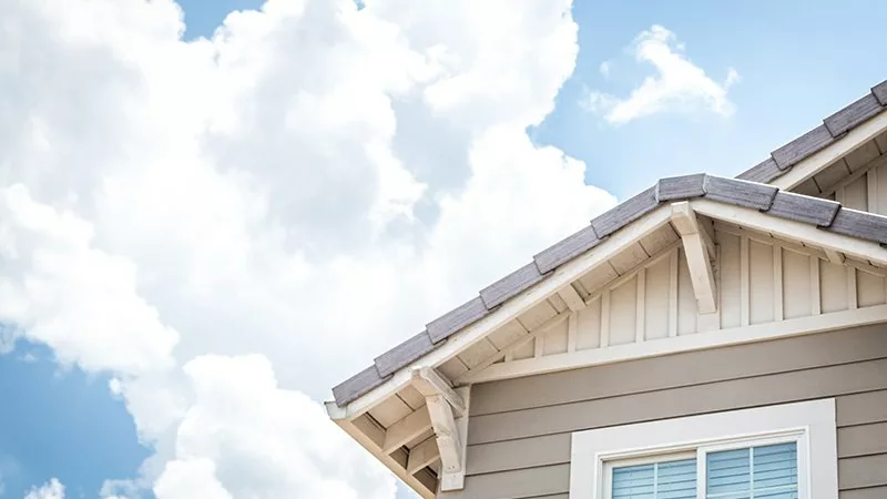 looking up at the second story of a house with blue sky and clouds behind it