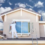 professional painter on roof of home painting the trim with white paint