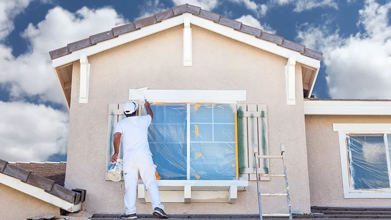 professional painter on roof of home painting the trim with white paint