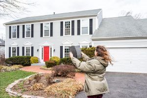 A woman standing outside of her home holding up paint samples on a windy day