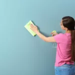 Young woman with long brown hair in pony tail cleaning a blue wall with a cloth