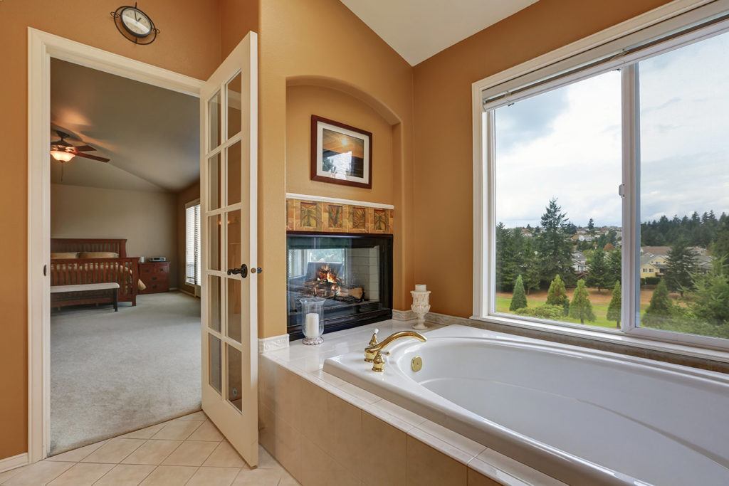 bathroom with gas fireplace and large window painted in warm tan earth tone
