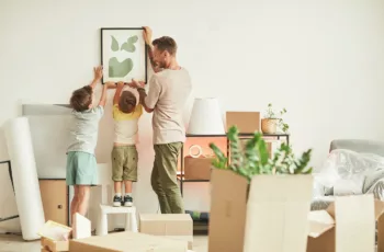Man and two children hanging picture in new home, with unpacked boxes in foreground.