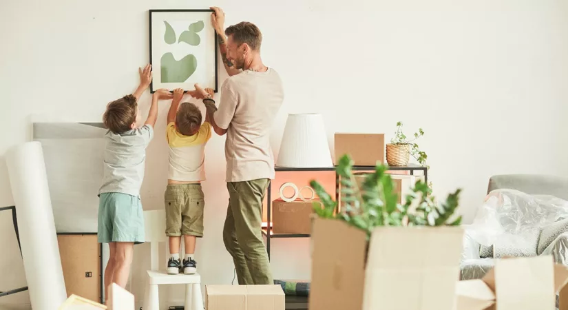 Man and two children hanging picture in new home, with unpacked boxes in foreground.