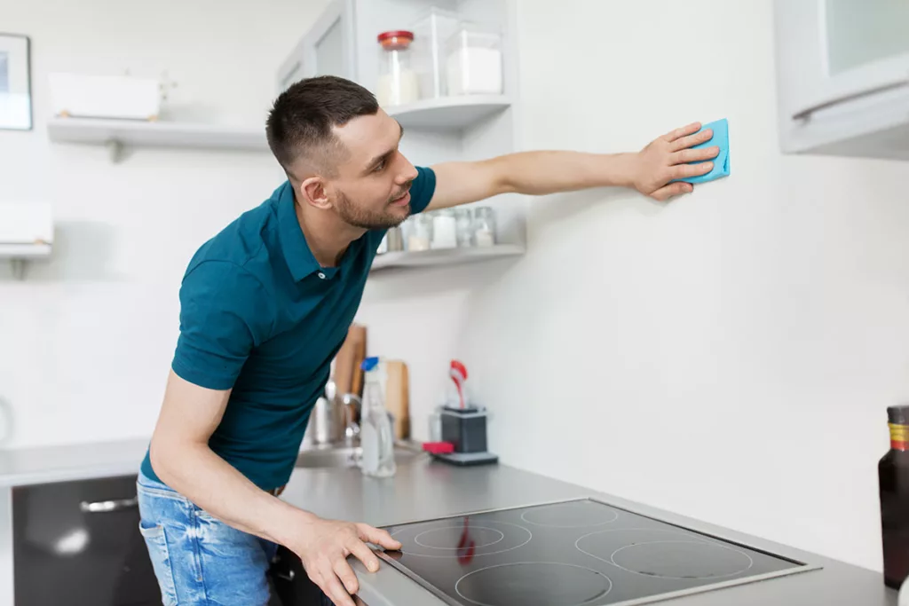 man cleaning wall above stovetop