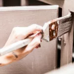 woman's hand painting kitchen cupboard with a small paint brush.