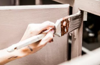woman's hand painting kitchen cupboard with a small paint brush.
