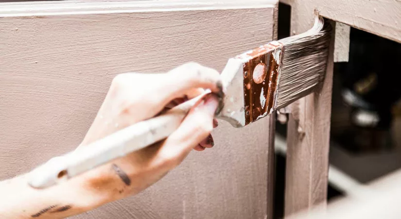 woman's hand painting kitchen cupboard with a small paint brush.