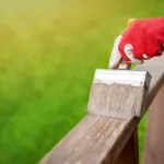 painter's gloved hand painting porch railing with a paint brush.