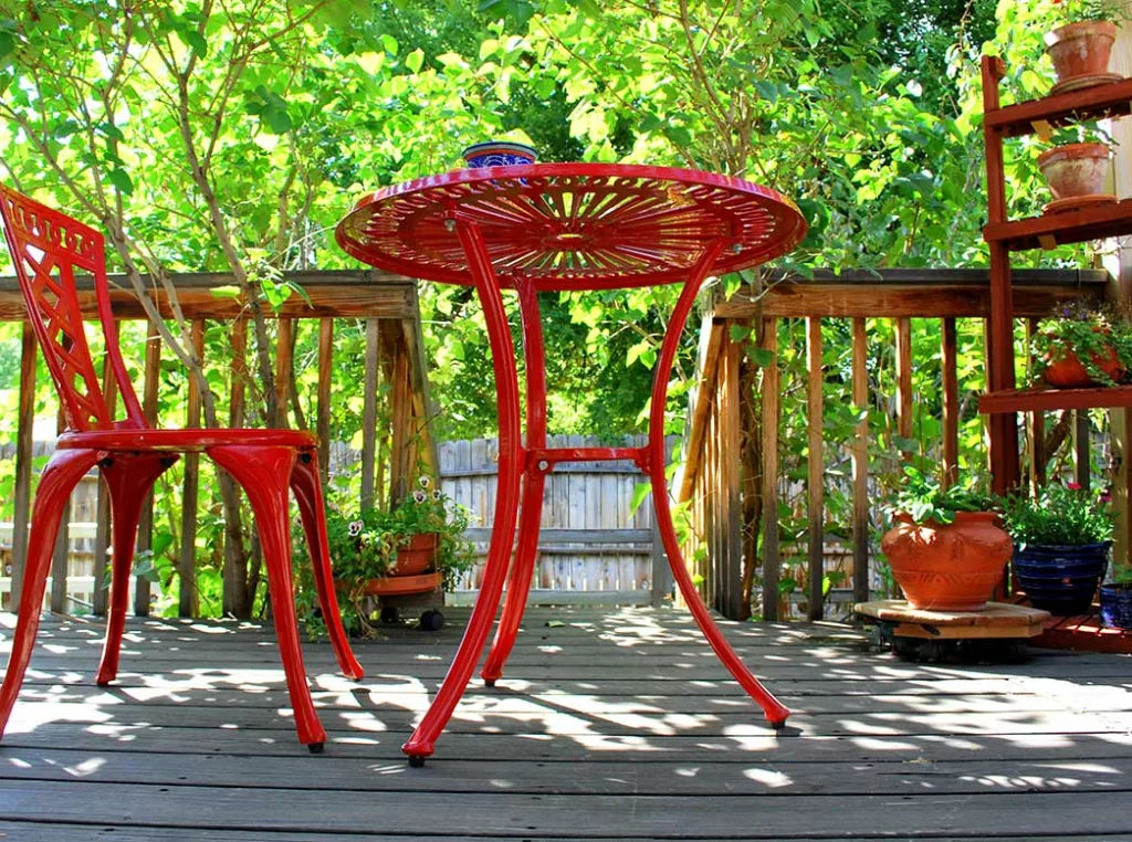 Red, rod-iron deck furniture. A cafe table and chair at the top of grey wooden deck
