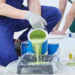 A commercial painter carefully pours green paint into a tray preparing for a commercial painting project
