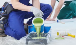 A commercial painter carefully pours green paint into a tray preparing for a commercial painting project