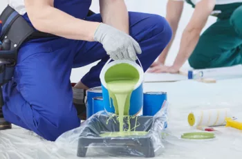 A commercial painter carefully pours green paint into a tray preparing for a commercial painting project