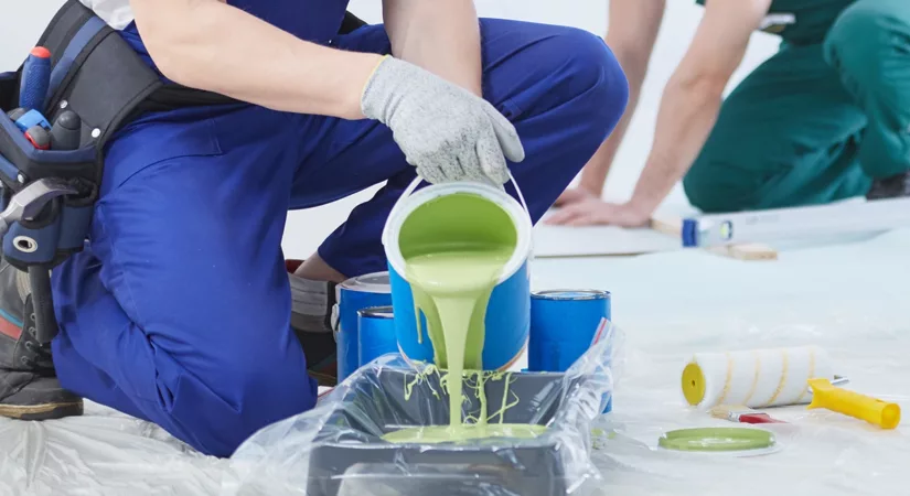 A commercial painter carefully pours green paint into a tray preparing for a commercial painting project