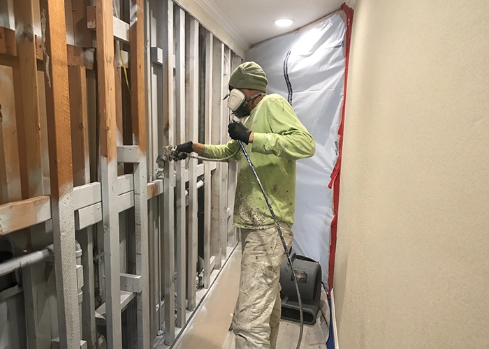 A professional residential painter applying a high-quality, moisture and mold-resistant paint primer to the entire surface area and the interior framing of a wall.