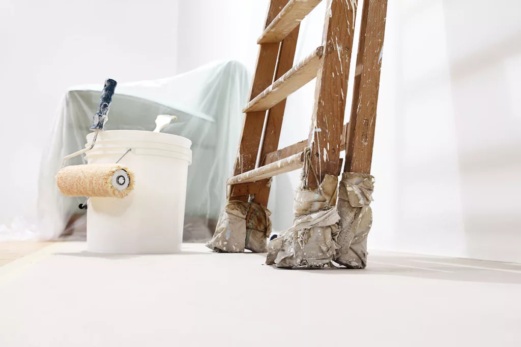 A living room with white walls, paint buckets, and a ladder is prepped for professional residential painting.