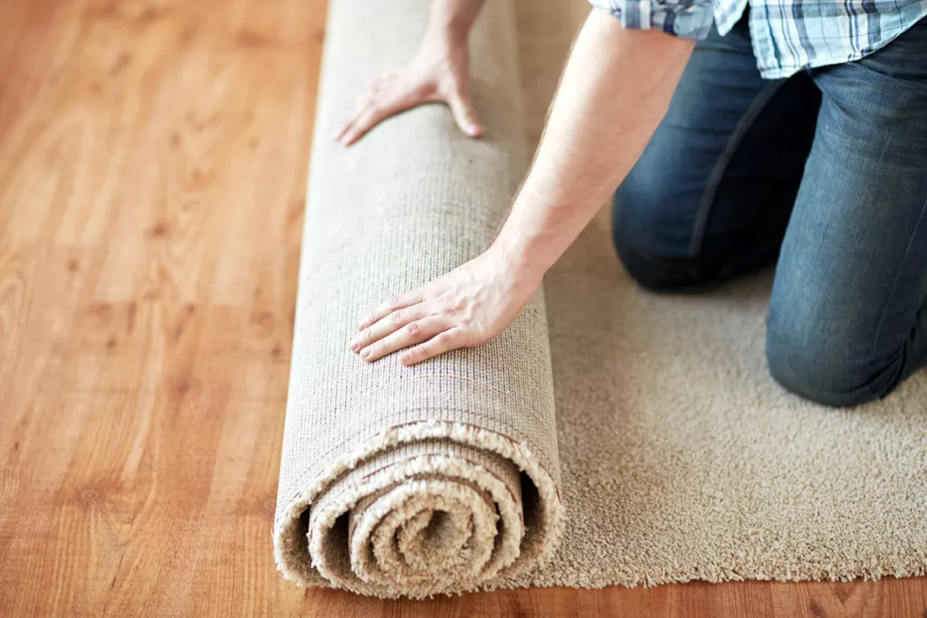 A close up of a man rolling up a beige rug to prep his home for professional residential painting.