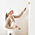 A professional painter uses a roller to paint interior walls white.