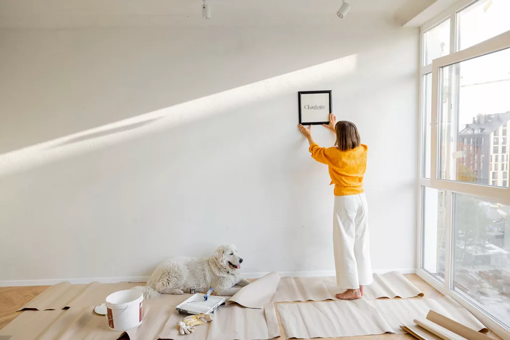A woman in a yellow shirt in an empty room removes the decor from walls to prep her home for professional residential painting.