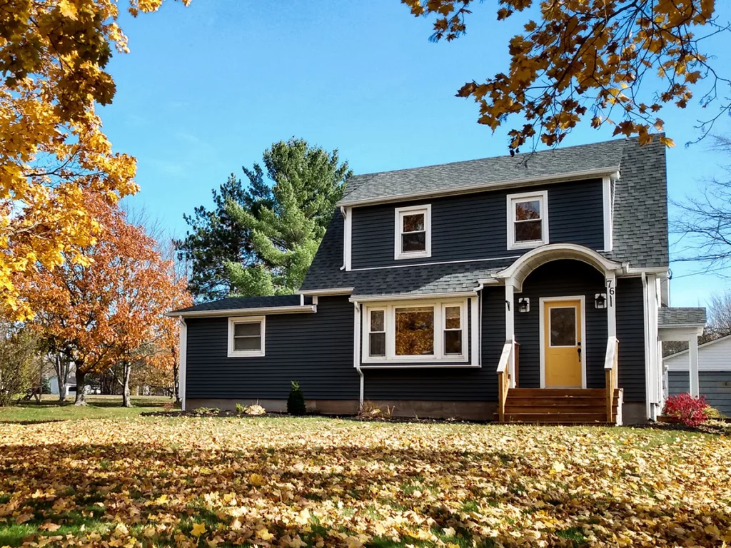 A house with dark black exterior paint and a yellow door in autumn, surrounded by fall foliage