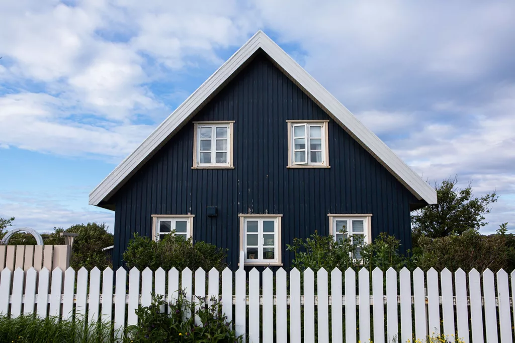 A house with dark blue exterior paint and a white fence