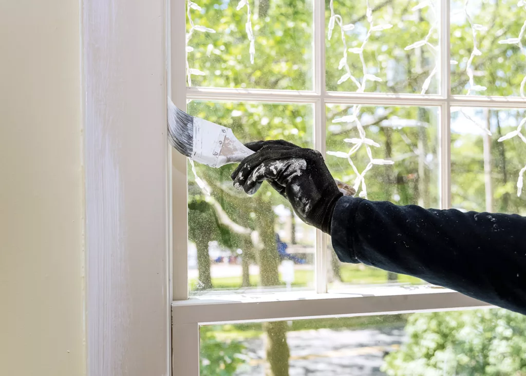 A professional residential painter repaints the interior trim around a window.