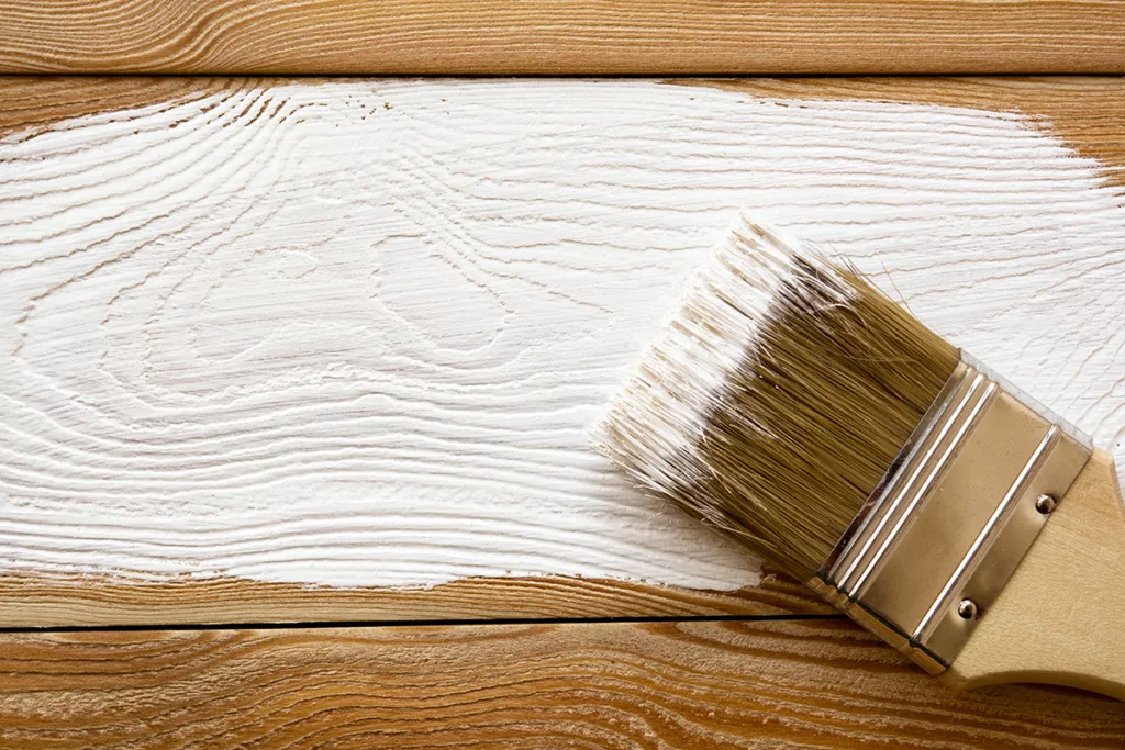 A paintbrush against the exterior of a house that is being painted white