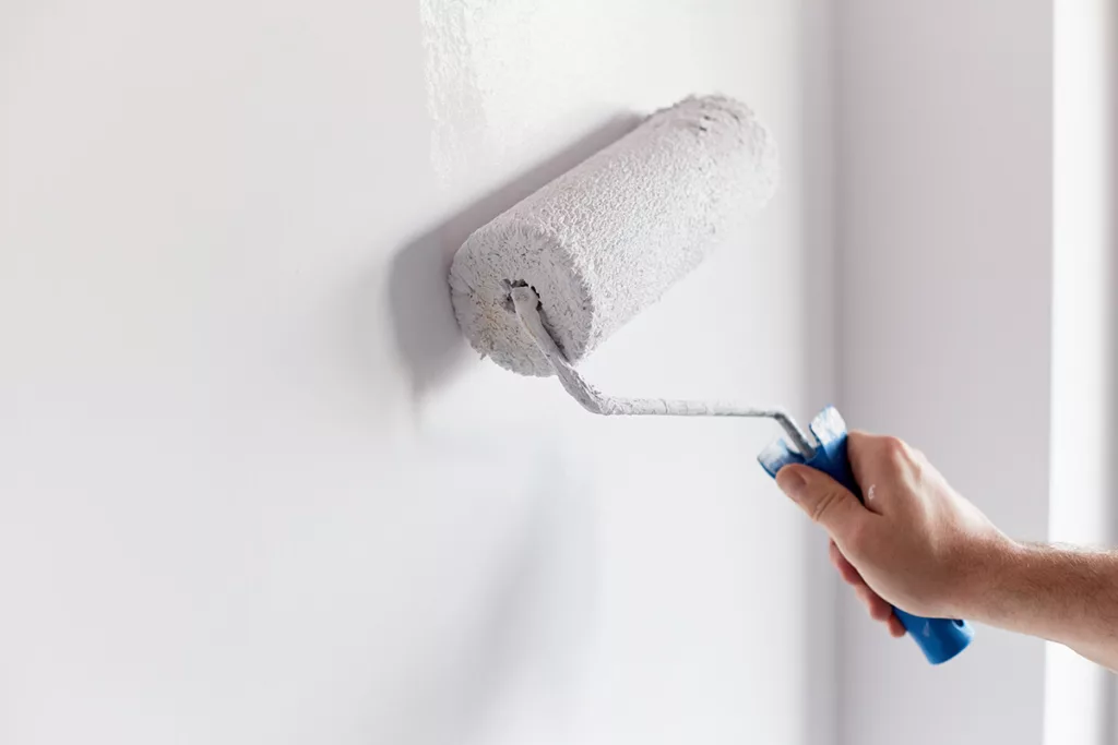 A professional residential painter uses a paint roller to paint a wall white.