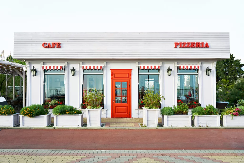 The exterior of a cafe and pizzeria after a commercial painting project, with white walls and red accents
