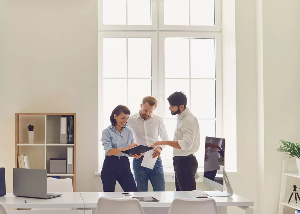 Three people stand around a desk in an office with white walls after a commercial painting project