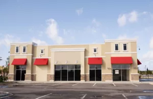 The exterior of a commercial building with professionally painted beige walls and red awnings.
