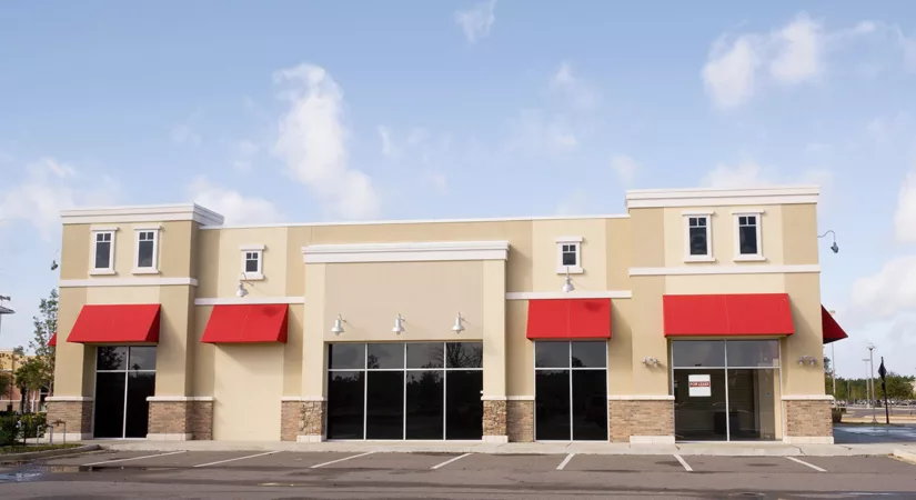 The exterior of a commercial building with professionally painted beige walls and red awnings.