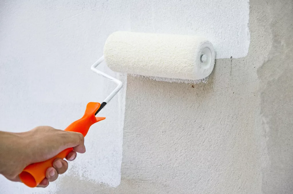 A painter applies paint sealer to a stone wall with a roller.