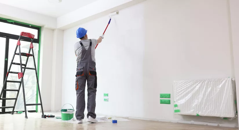 A professional residential painter primes the interior wall of a house with a long paint roller.