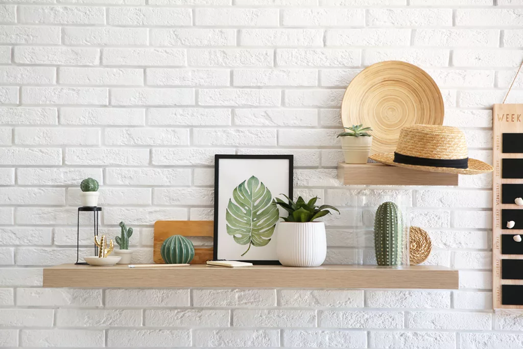 An interior brick wall painted white, with floating shelves, decorations, picture frames, and plants.