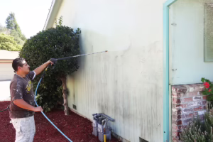 A professional residential painter pressure rinsing the exterior wall of a white house