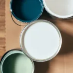 A birds-eye shot of open paint cans on a wooden floor in muted colors, showing the concept of how to choose the best type of paint for different surfaces
