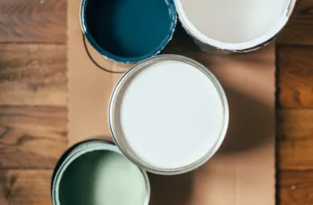 A birds-eye shot of open paint cans on a wooden floor in muted colors, showing the concept of how to choose the best type of paint for different surfaces