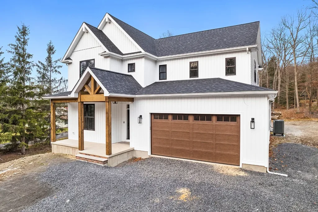 The exterior of a house in the woods with white eggshell paint and a brown garage door