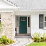 The front of a house with white brick, black shutters, and a green door, showing the concept of how to choose the best exterior paint finish for your home