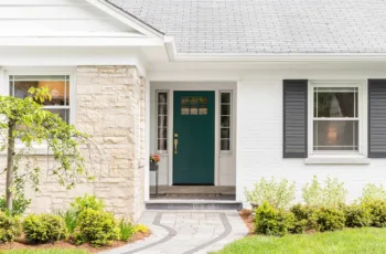 The front of a house with white brick, black shutters, and a green door, showing the concept of how to choose the best exterior paint finish for your home