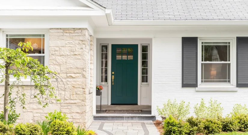 The front of a house with white brick, black shutters, and a green door, showing the concept of how to choose the best exterior paint finish for your home