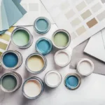 A birds-eye shot of a variety of interior and exterior paint cans, on an flatlay of color palettes and papers