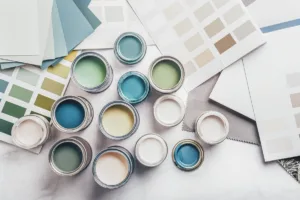 A birds-eye shot of a variety of interior and exterior paint cans, on an flatlay of color palettes and papers