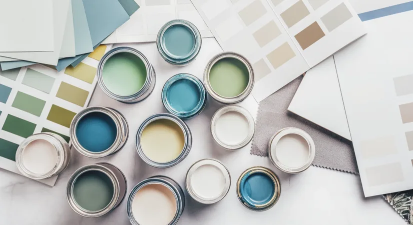 A birds-eye shot of a variety of interior and exterior paint cans, on an flatlay of color palettes and papers